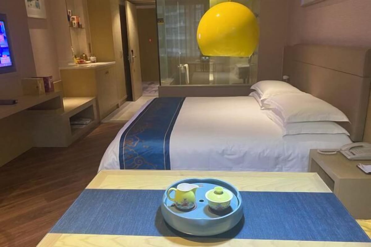 A hotel room with a bed, bedside table, and a tray with a teapot and cup.