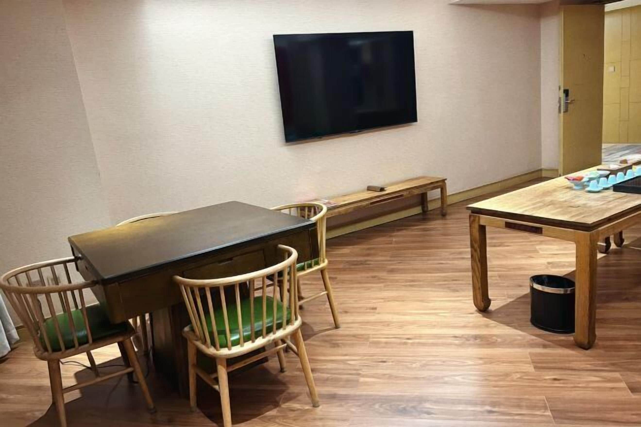 A room with a wooden table, two chairs, a bench, a television on the wall, and a trash can.