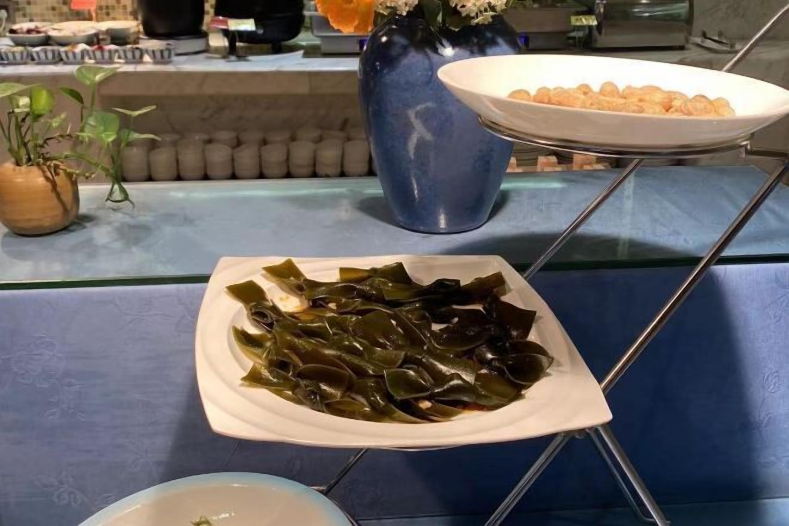 A dining area with a white plate of seaweed and a bowl of small round items on a glass table.