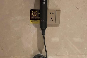 A power strip with a cable plugged in, mounted on a wall with a visible electrical outlet. - Richun Teaism Hotel (Quanzhou)