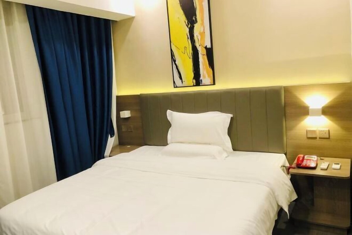 A hotel room with a bed, a nightstand, a telephone, and a painting on the wall.
