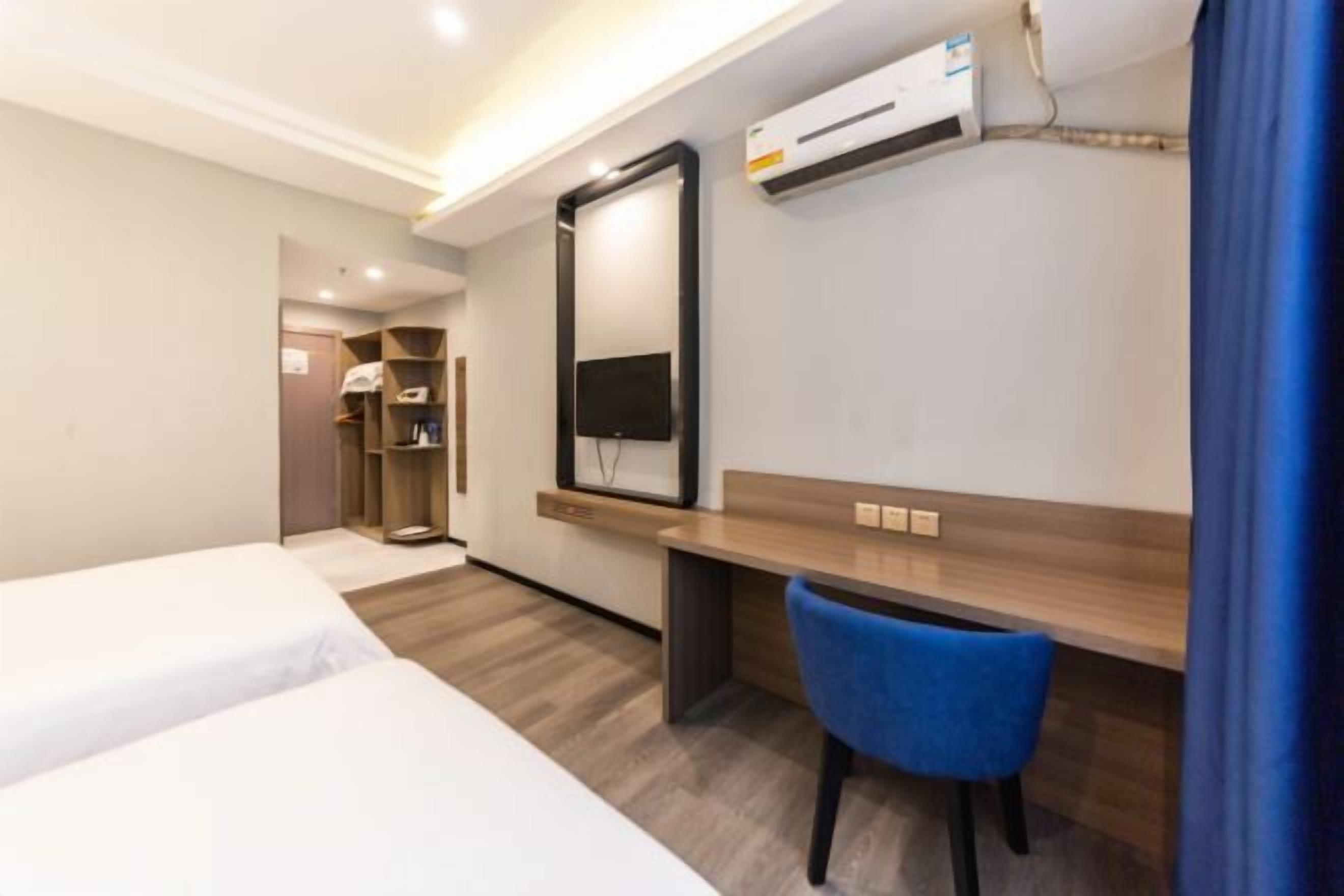 Quarto de hotel com duas camas, uma escrivaninha, uma cadeira, uma televisão e um ar condicionado.