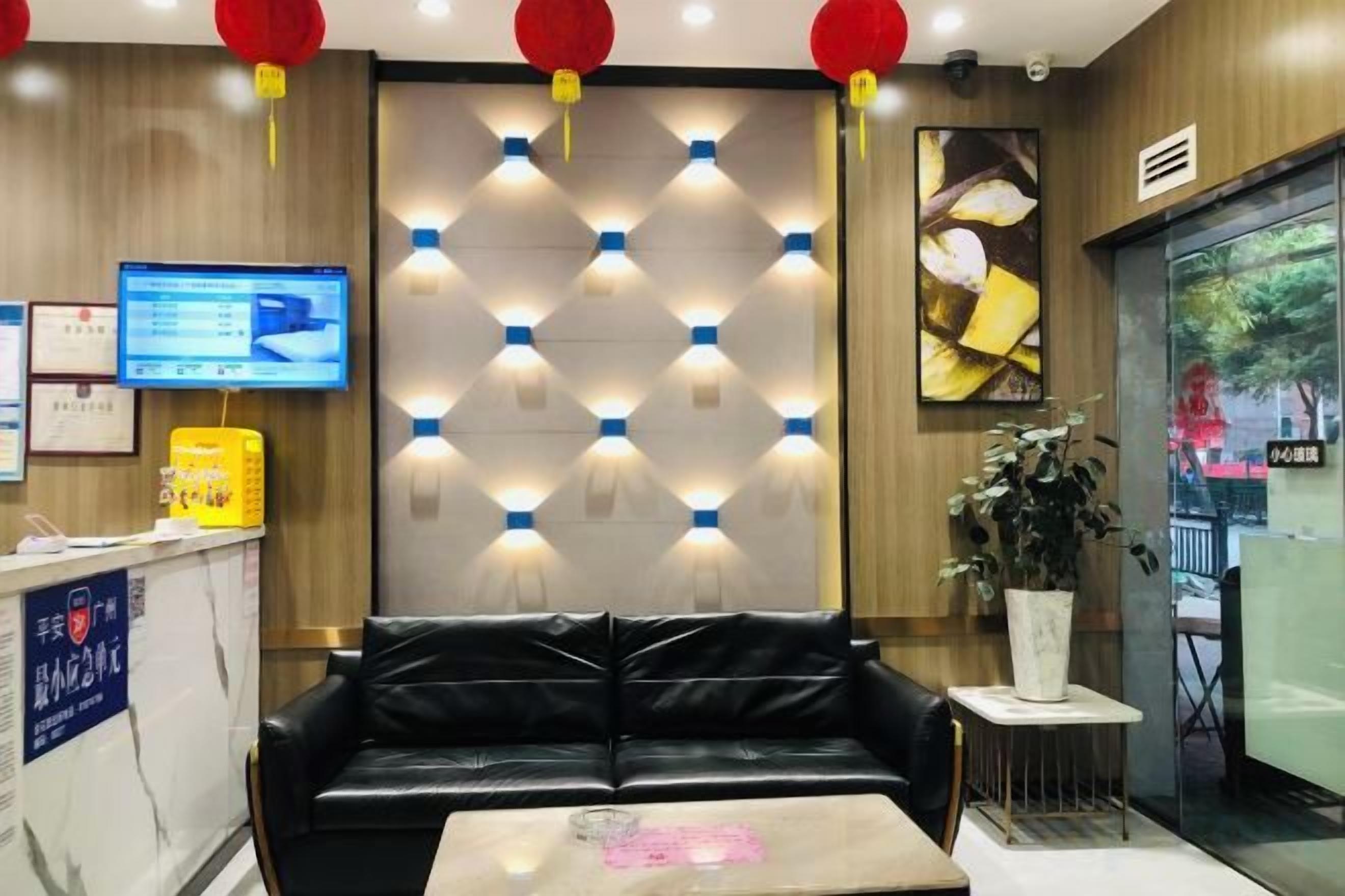 A hotel lobby with a black leather sofa, a reception desk, and a wall-mounted light fixture.