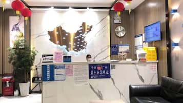 Zona de recepción de hotel con mostrador de mármol, un reloj, una televisión y un área de descanso.