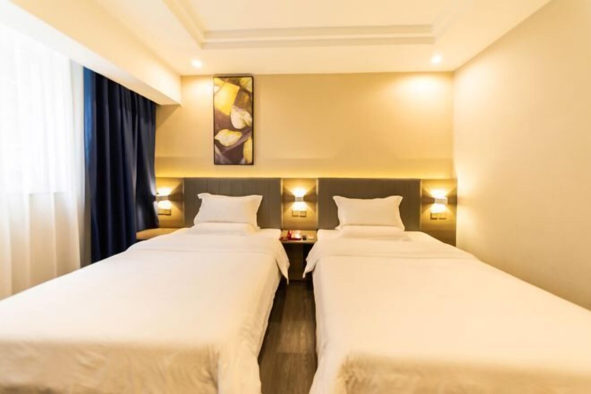A hotel room with two beds, a nightstand between them, and a wall-mounted light fixture above.