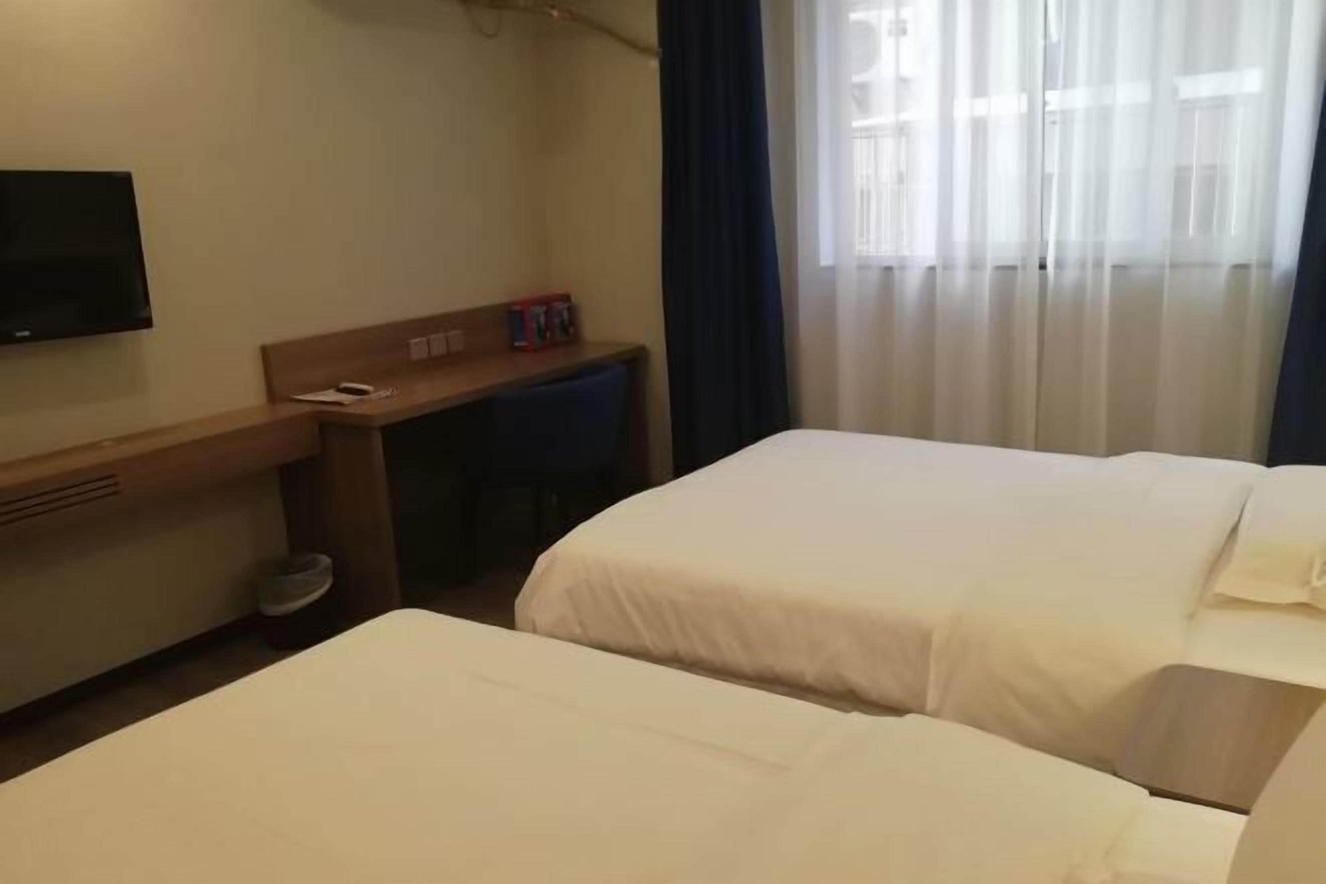 Ein Hotelzimmer mit zwei Betten, einem Schreibtisch, einem Fernseher und einem Fenster mit Vorhängen.