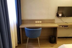 Ein Hotelzimmer mit einem Holztisch, einem blauen Stuhl, einem an der Wand befestigten Fernseher und einer kleinen Mülltonne.
