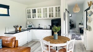 Cozinha moderna com armários brancos, geladeira preta e mesa de jantar de madeira.