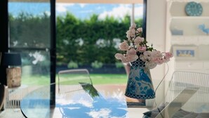 Uma mesa com um vaso de flores, uma cadeira e vista para o verde lá fora.