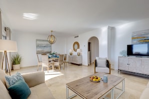A modern living room with a sofa, coffee table, dining area, and TV.