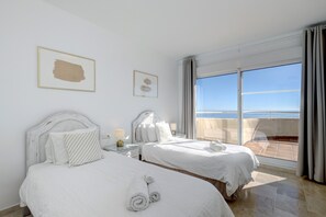 A hotel room with two beds, a balcony with a view, and a large window.