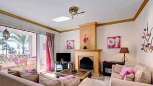 A living room with a sofa, television, fireplace, and balcony with chairs.