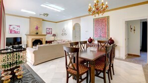 A dining area with a chandelier, a fireplace, and a sofa in a well-lit room with a tiled floor.