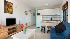 A living room with a TV, wooden cabinet, and a blue sofa. - Mirra Apartment – Beach View (Puerto Rico)