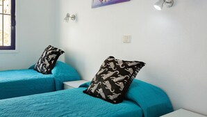 A room with two beds, each with a teal bedspread and a black pillow with white animal prints. There is a wall-mounted light fixture and a painting above the beds. - Mirra Apartment – Beach View (Puerto Rico)
