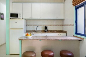 A kitchen with a microwave, refrigerator, sink, and a fruit bowl on the counter.