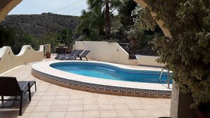 Ein Swimmingpool mit Liegestühlen, umgeben von einer gefliesten Terrasse und Blick auf eine gebirgige Landschaft.