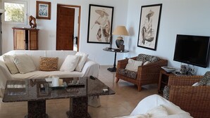Ein Wohnzimmer mit einer Couch, Sesseln, einem Couchtisch, einem Fernseher und Kunstwerken an der Wand.
