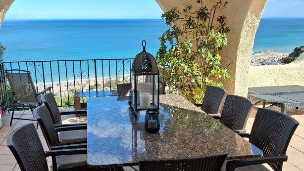 Eine Terrasse mit Tisch und Stühlen, einer Laterne und Blick auf den Ozean.