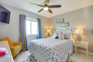 Un dormitorio con cama, ventilador de techo, televisión y ventana con cortinas.