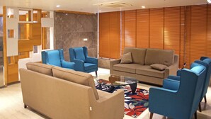 Una sala de estar moderna con un sofá color beige, sillones azules y una mesa de centro de vidrio.
