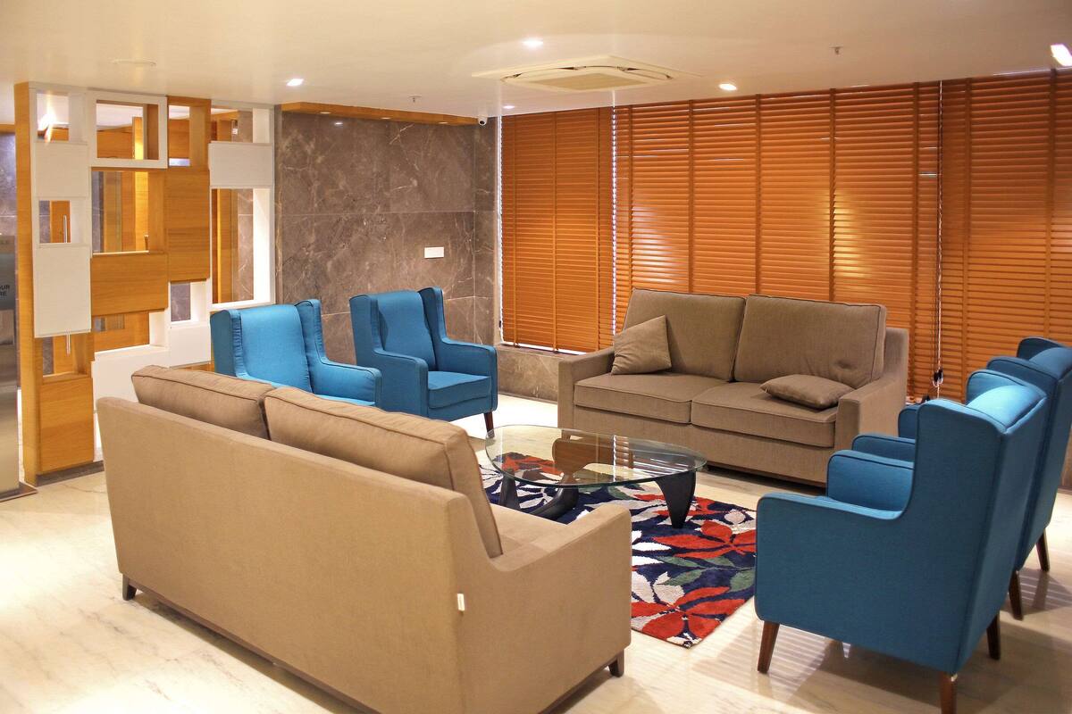 A modern living room with a beige sofa, blue armchairs, and a glass coffee table.