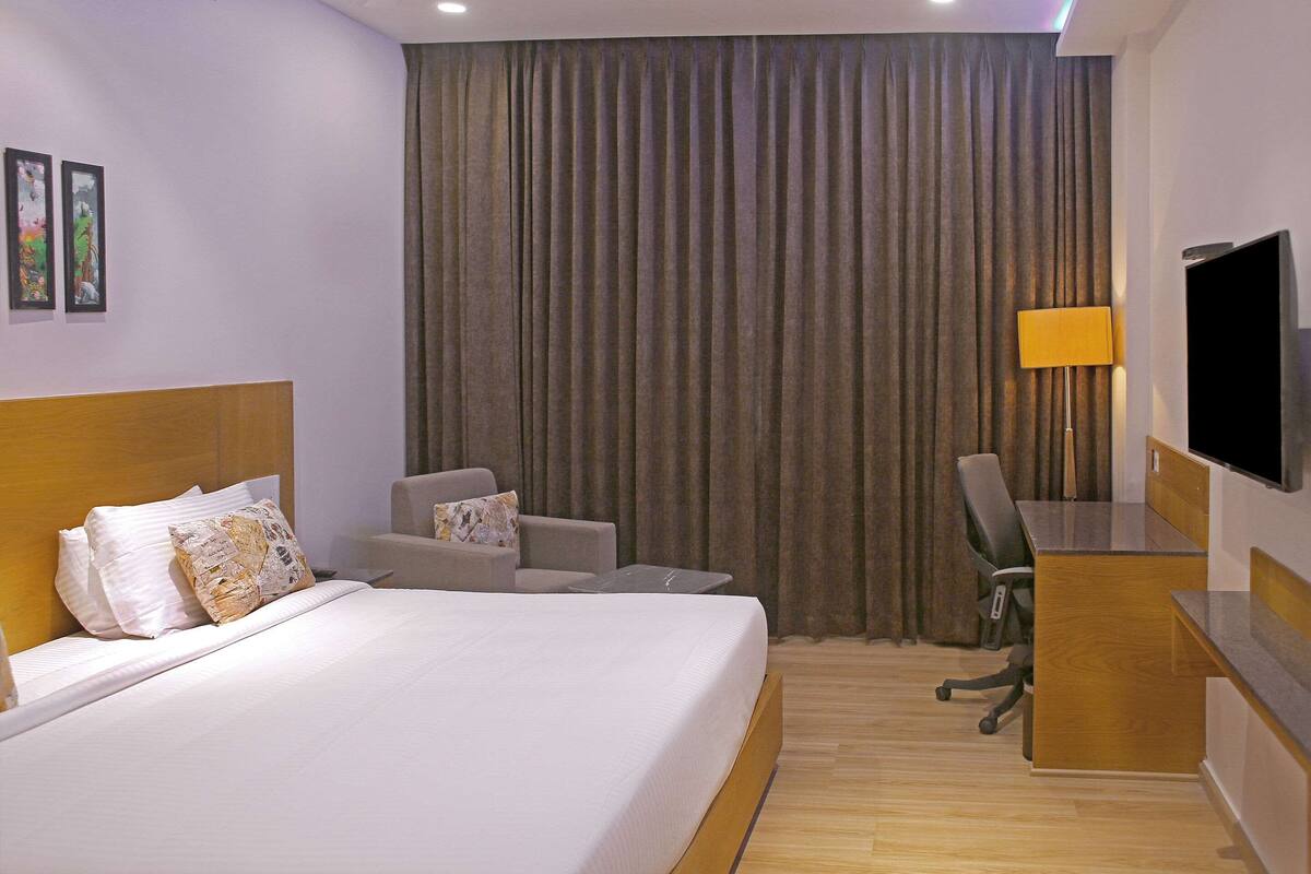 A hotel room with a large bed, a desk, a chair, a TV, and a curtain.