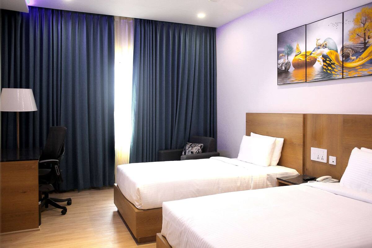 A hotel room with two beds, a desk, a chair, a lamp, and a painting on the wall.