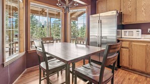 A kitchen with wooden cabinets, a stainless steel refrigerator, a microwave, and a dining table with chairs. - Hikers Haven - Close to Hiking, Fireplace, Horseshoes, Deck, BBQ (Big Bear City)