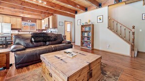 A spacious living room with a leather sofa, a wooden chest, and a bookshelf. - Hikers Haven - Close to Hiking, Fireplace, Horseshoes, Deck, BBQ (Big Bear City)