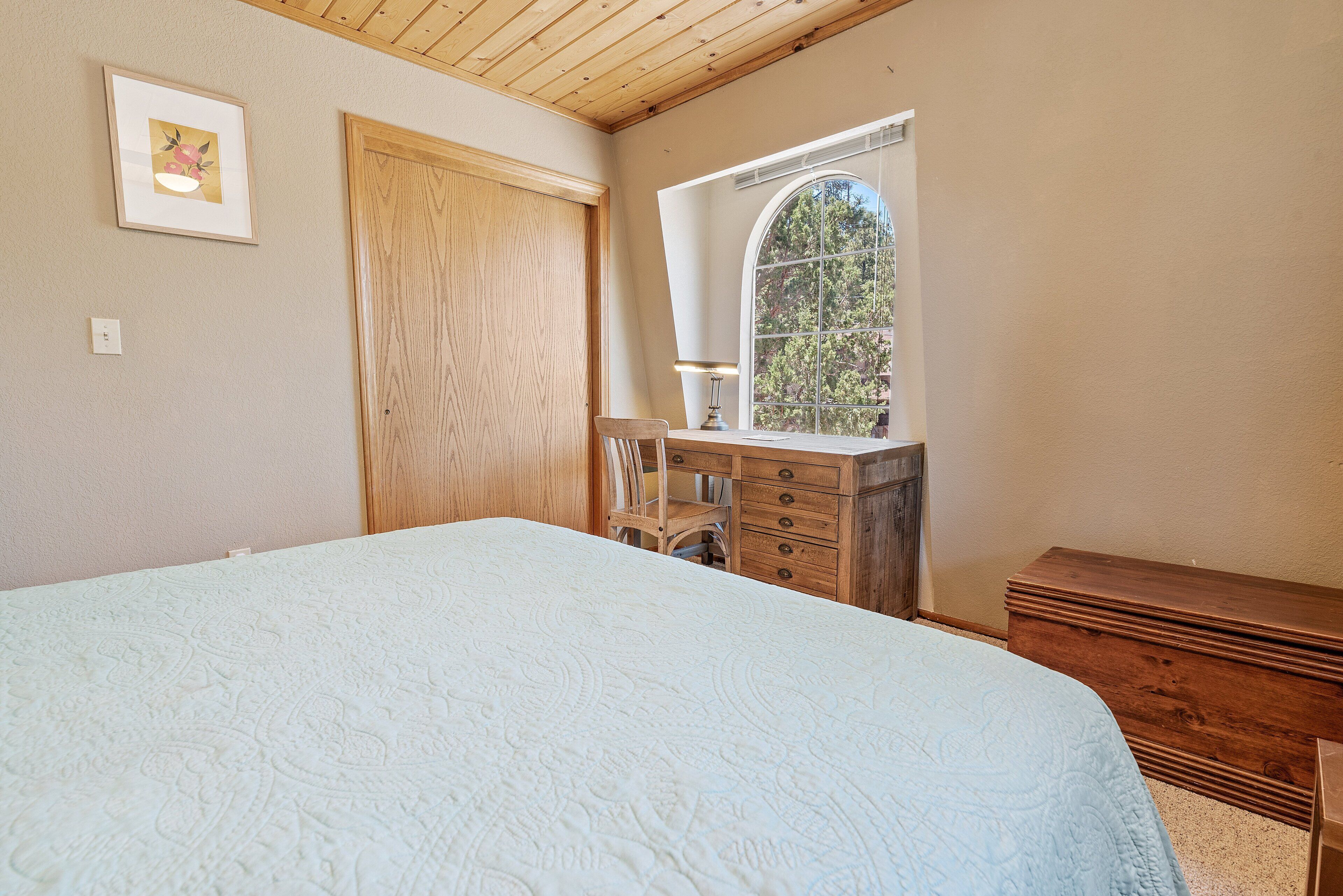 A bedroom with a large bed, wooden dresser, and a window with a view of trees.