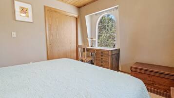 A bedroom with a large bed, wooden dresser, and a window with a view of trees.