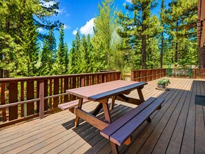 A wooden deck with picnic tables and benches, surrounded by trees.