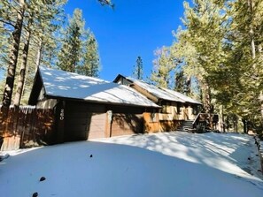 A cabin with a snow-covered roof, surrounded by tall pine trees.