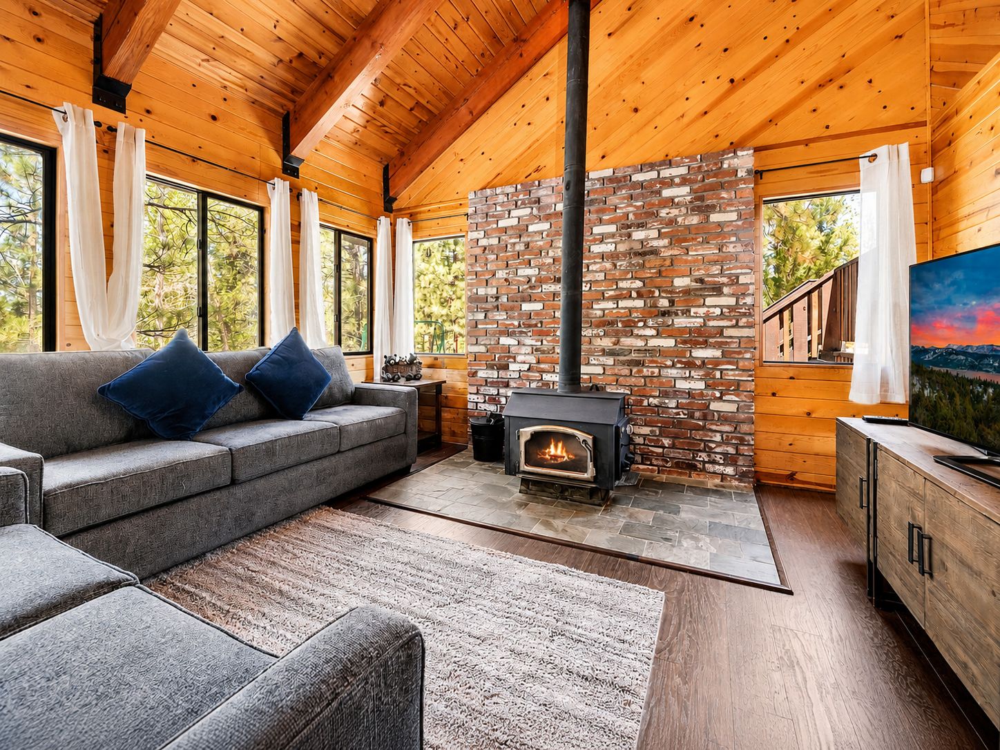 A cozy cabin interior with a fireplace, wooden walls, a sofa, and a television.