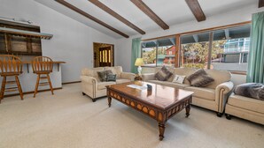 A living room with a wooden coffee table, two armchairs, a sofa, and a dining area with wooden chairs.