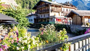 A riverside view of a traditional wooden building with balconies, surrounded by lush greenery and mountains in the background. - Modern Mountain Stay (Abondance)