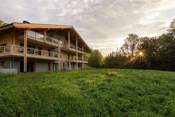 A multi-story building with balconies, set on a grassy hill with trees in the background. - Modern Mountain Stay (Abondance)