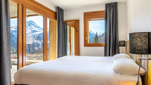 A hotel room with a large bed, a window with a mountain view, and a lamp. - Modern Mountain Stay (Abondance)