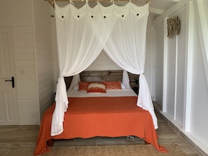 A bed with a white canopy and orange bedding, wooden headboard, and a woven rug on the floor. - Beautiful Villa with Sea View & Pool - Relaxing stay in the tropics (Deshaies)