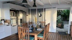 Una cucina moderna con mobili bianchi ed elettrodomestici in acciaio inossidabile, un tavolo da pranzo in legno con sedie, e vista su un giardino attraverso una porta aperta.