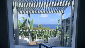 Un balcone con vista sull'oceano, sedie bianche e un pergolato.