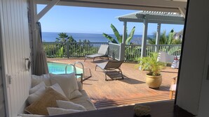 Un terrazzo in legno con piscina, sedie a sdraio e vista sull'oceano.
