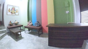 A room with a colorful striped wall, a wooden reception desk, a bench, and a small table. - Little Peepal House (Udaipur)