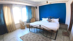 A bedroom with a bed, a chair, and a decorative rug. - Little Peepal House (Udaipur)