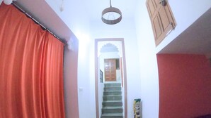 A hallway with a staircase, a red curtain, and a tiled floor. - Little Peepal House (Udaipur)