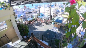 A rooftop terrace with tables and chairs, potted plants, and a view of the cityscape. - Little Peepal House (Udaipur)