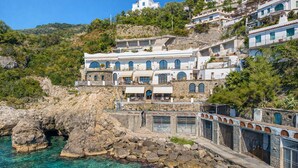 A coastal building with multiple balconies, a stone facade, and a view of the sea.