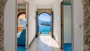 A corridor leading to a balcony with a stone wall and a view of the sea.