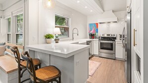 Une cuisine moderne avec des meubles blancs, un grand îlot central, des appareils en acier inoxydable et un dosseret orné d’un motif en chevrons.